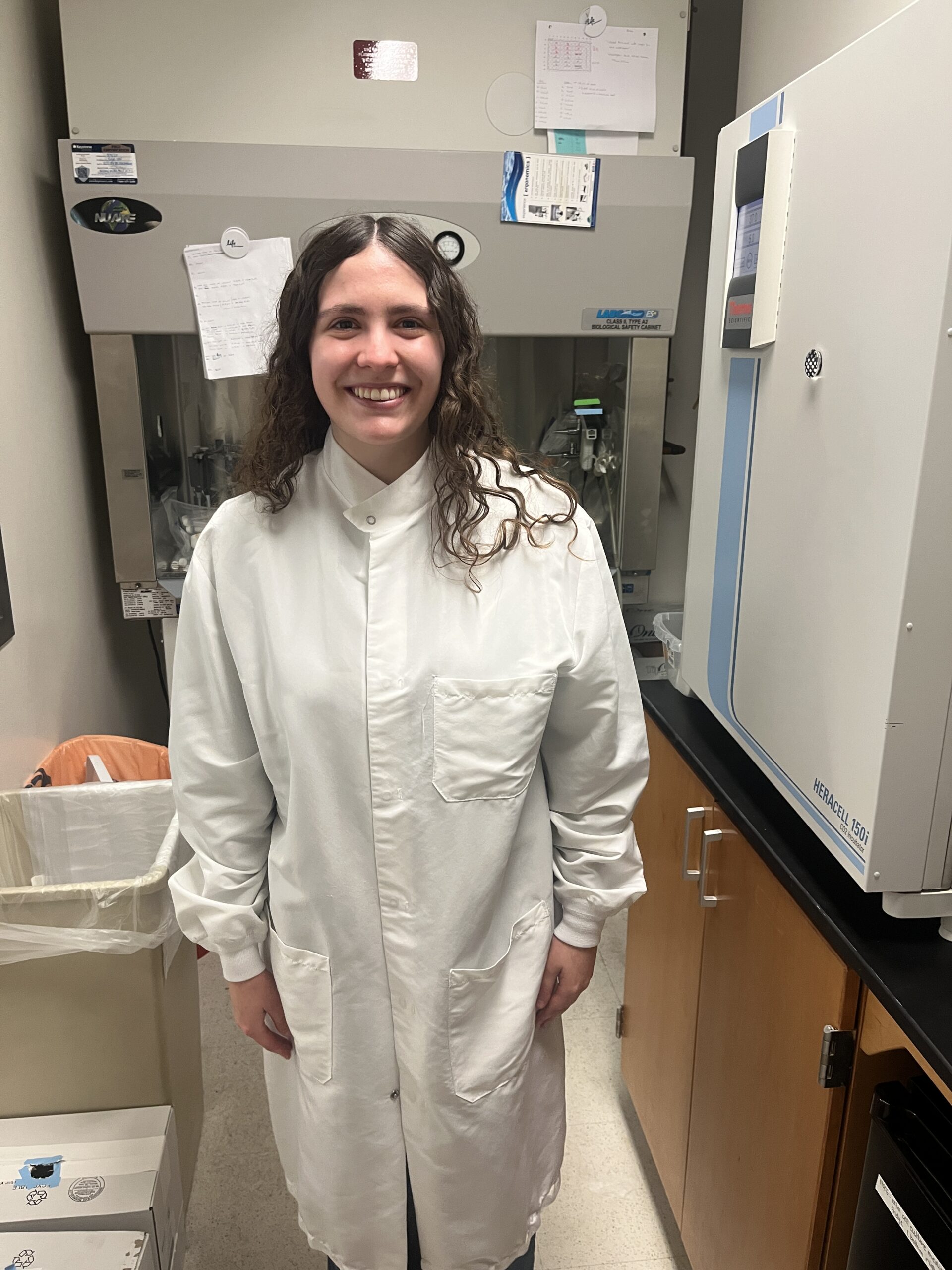 Student with curly hair wearing a lab coat standing in a cell culture room